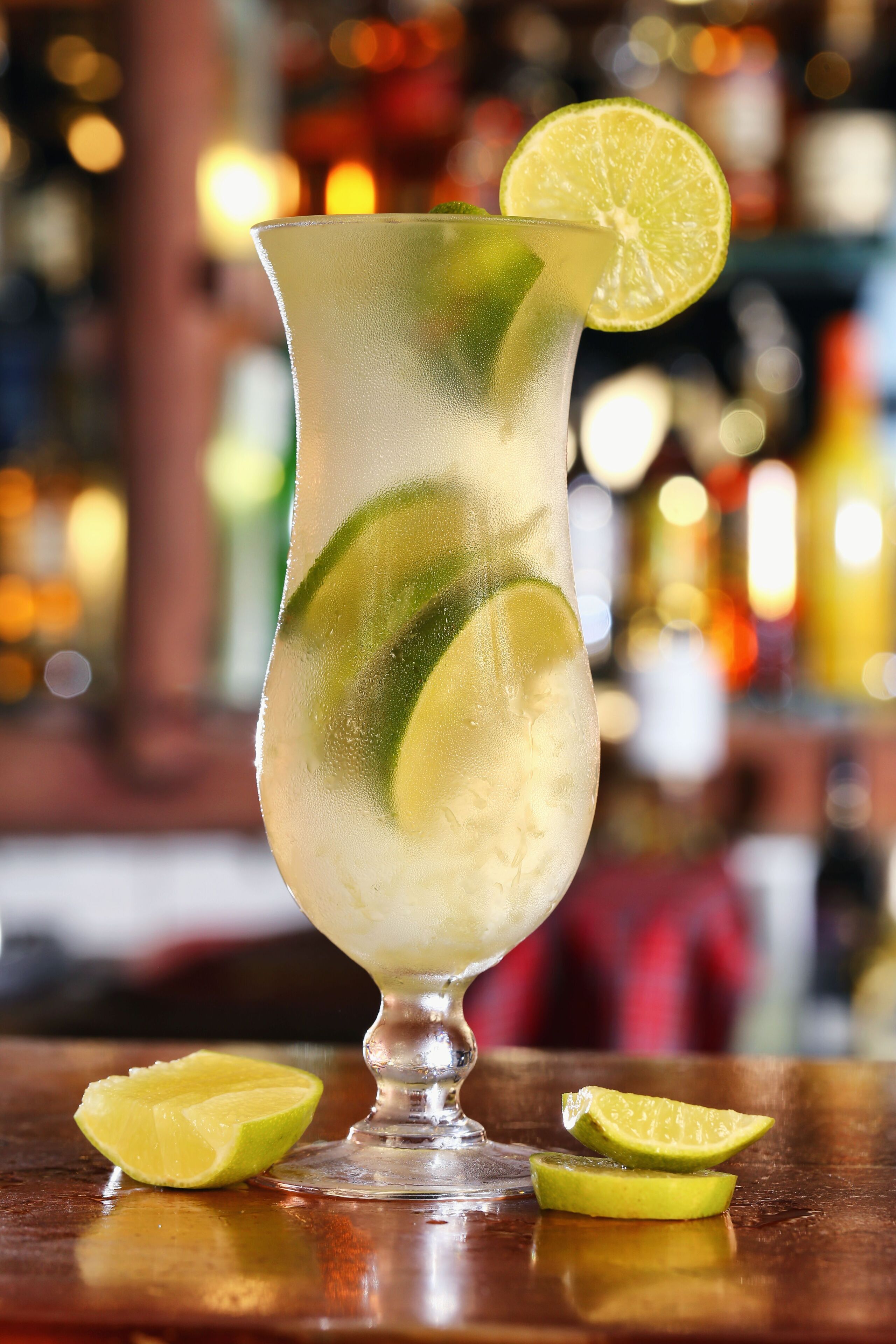 A cocktail glass with lime slices and a lime garnish on a bar counter.