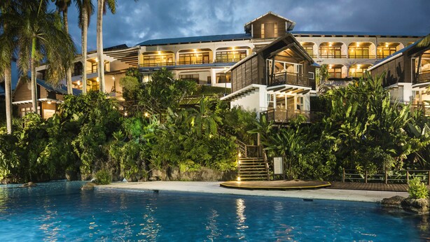 Un resort con piscina, palmeras y un edificio grande con varios balcones.