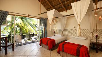 Habitación de hotel con dos camas, un balcón y vistas a palmeras.