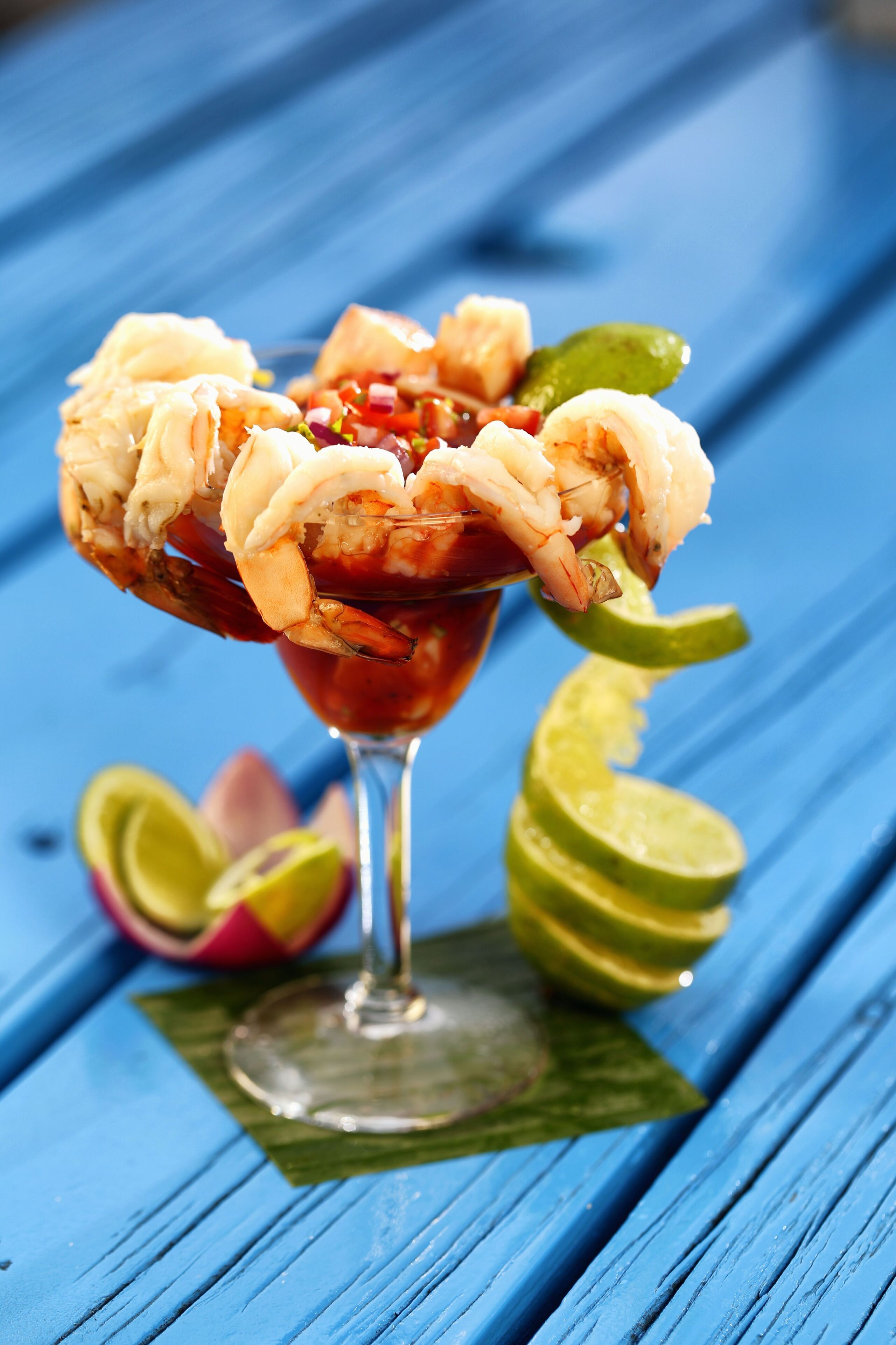 A shrimp cocktail in a glass with lime wedges and a slice of lime on a blue wooden surface.