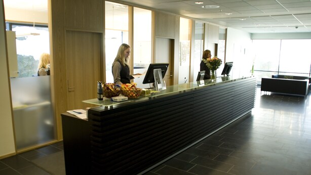 A reception desk with a computer monitor, a cash register, and a basket of snacks. - Hotell Montebello (Oslo)