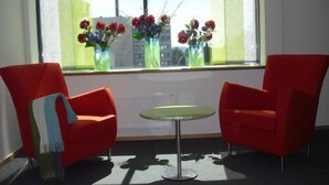 A room with two red chairs, a small round table, and a window with a view of buildings and flowers. - Hotell Montebello (Oslo)