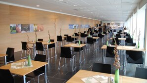 A spacious dining area with multiple tables and chairs, a wooden wall with artwork, and a modern ceiling design. - Hotell Montebello (Oslo)
