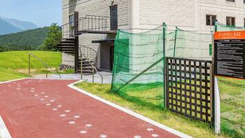 Una pista di atletica rossa con impronte bianche a zampa, un'area recintata verde per cani e un edificio con facciata in pietra.