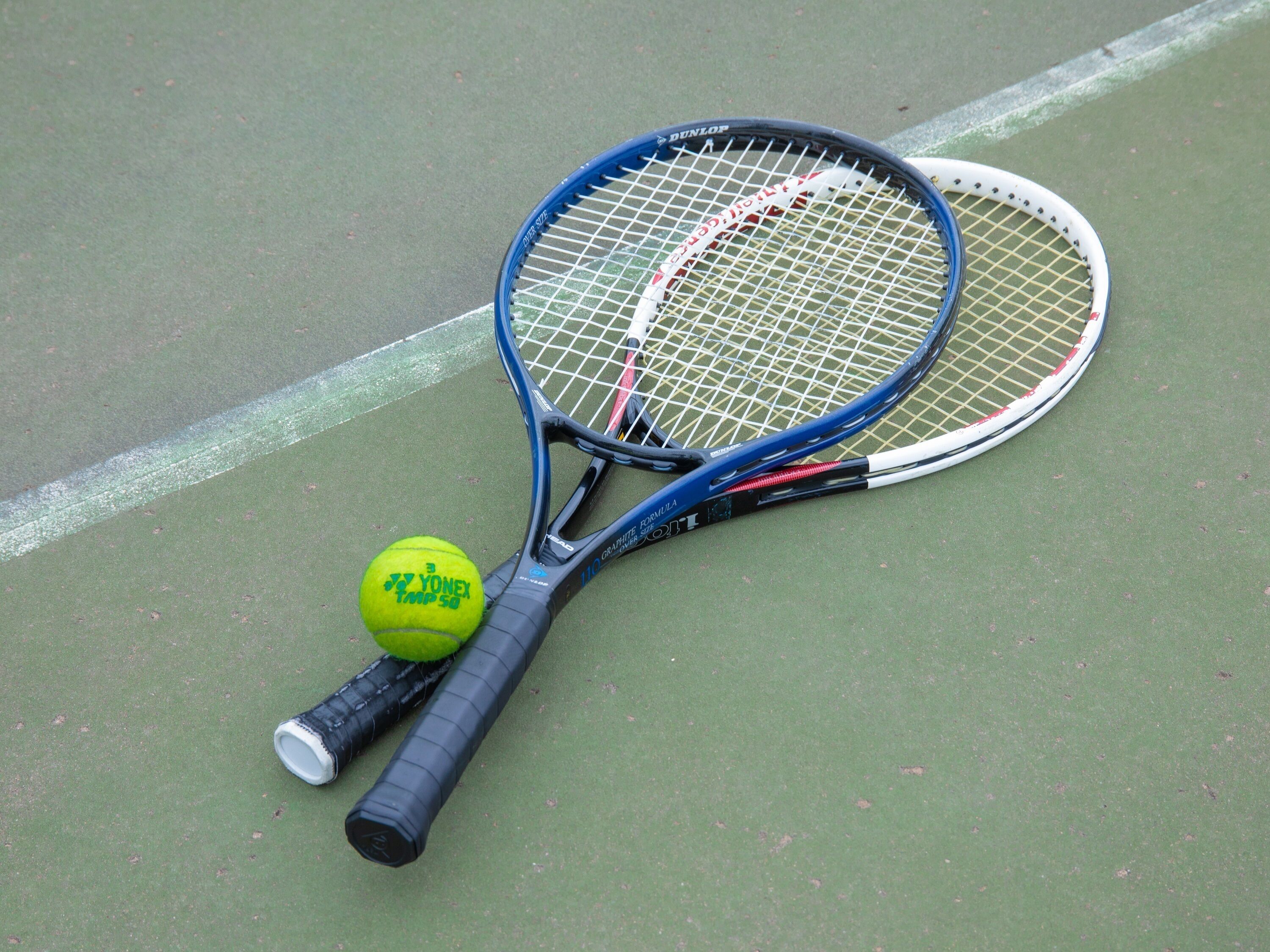 Two tennis rackets and a tennis ball on a green court.