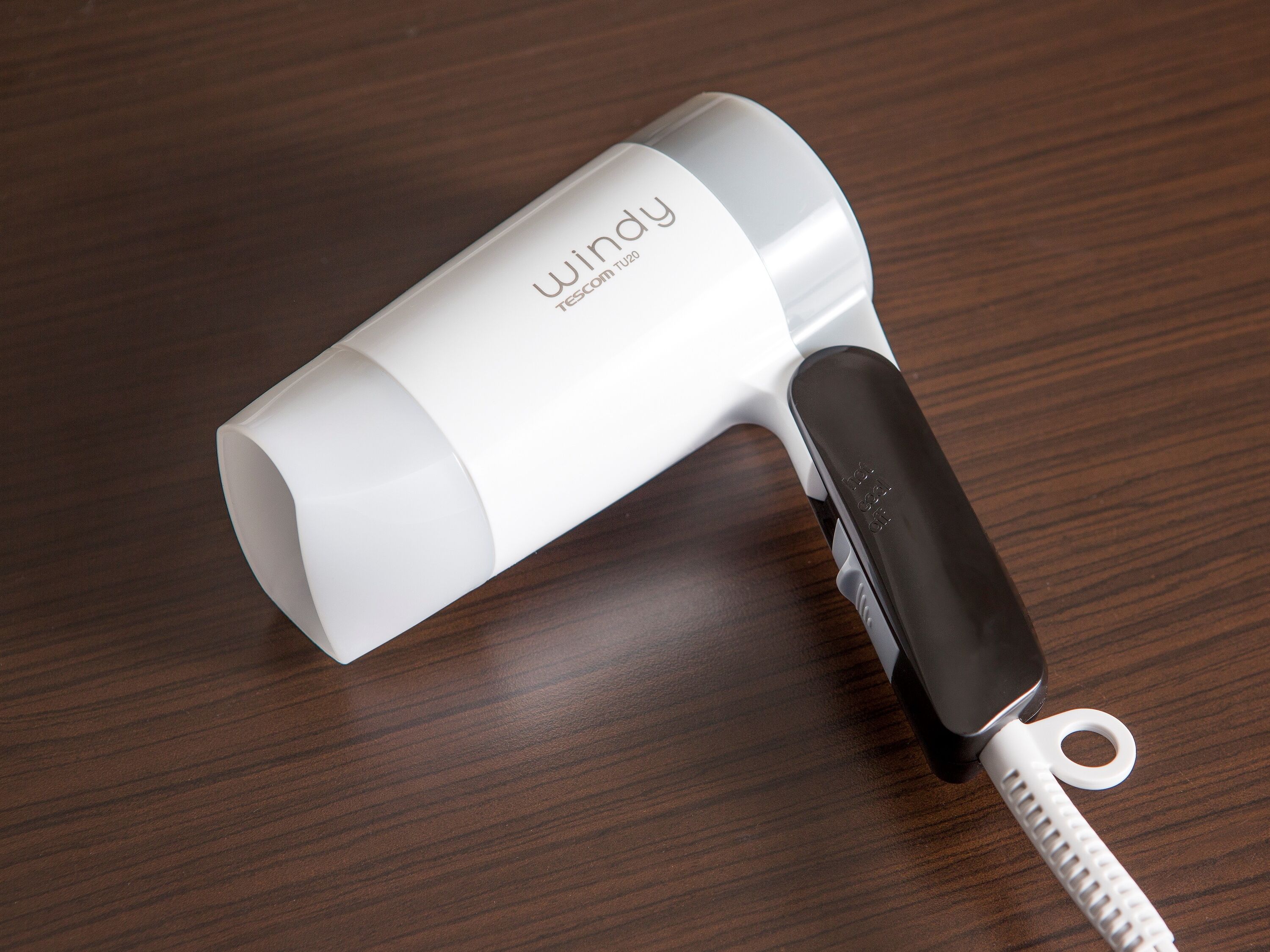 A white and black portable hair dryer with a compact design, placed on a wooden surface.