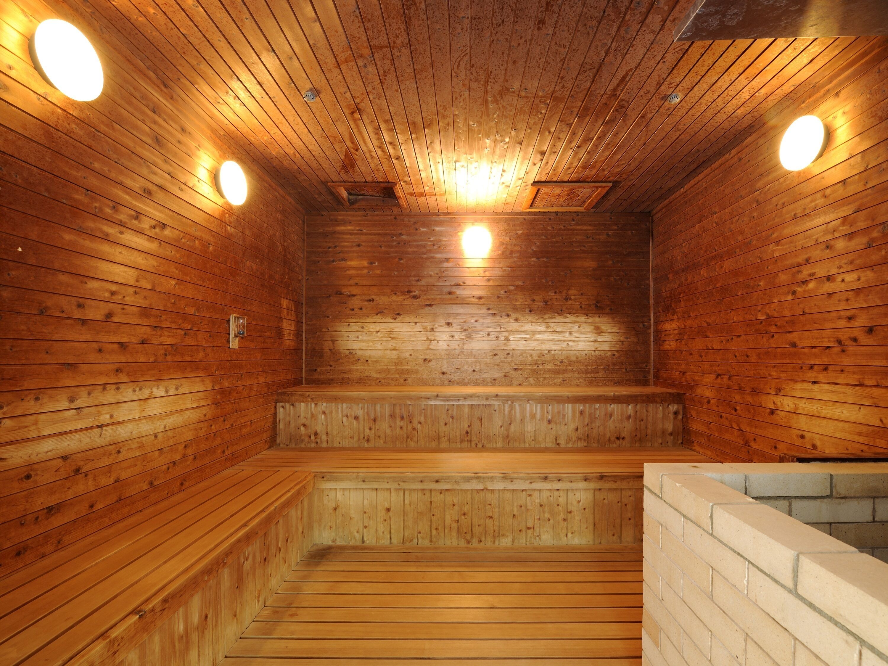 A wooden sauna with benches and a brick wall.