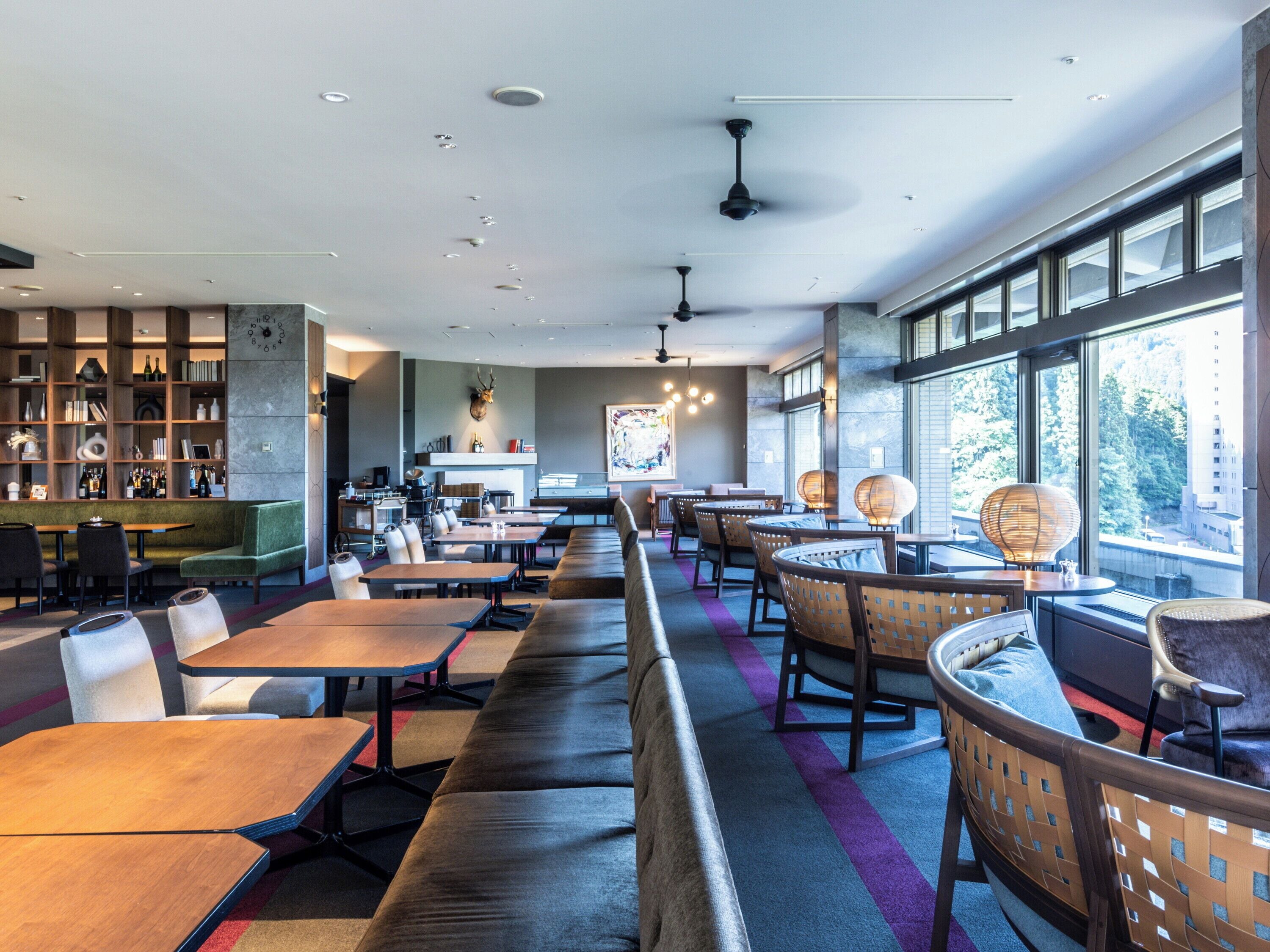 A modern restaurant with a long counter, booths, and a bookshelf.