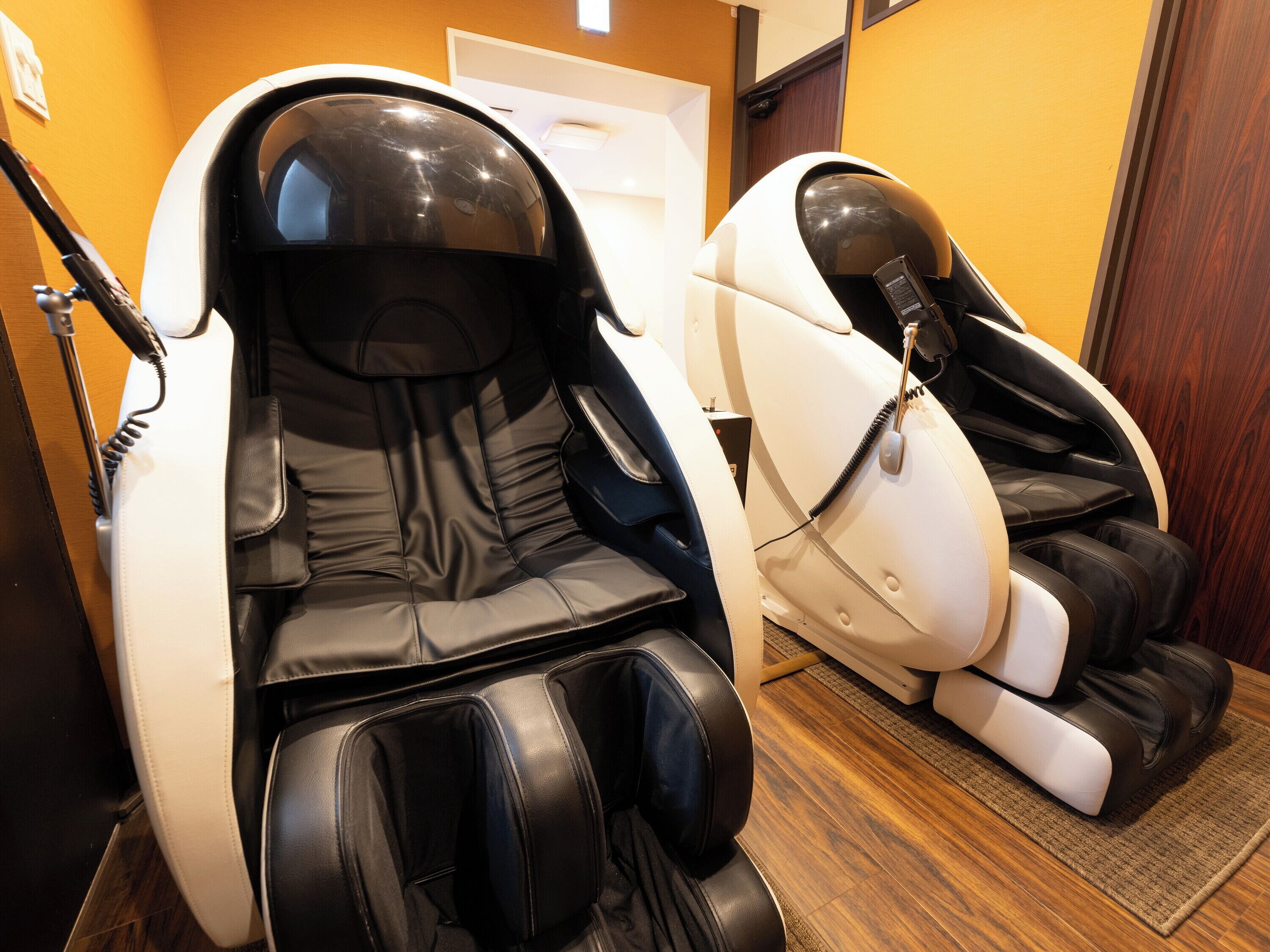 Two massage chairs in a room with wooden flooring and a door in the background.