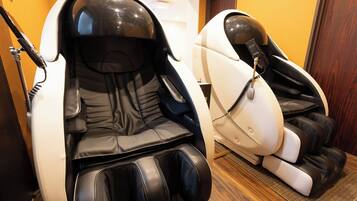 Two massage chairs in a room with wooden flooring and a door in the background.