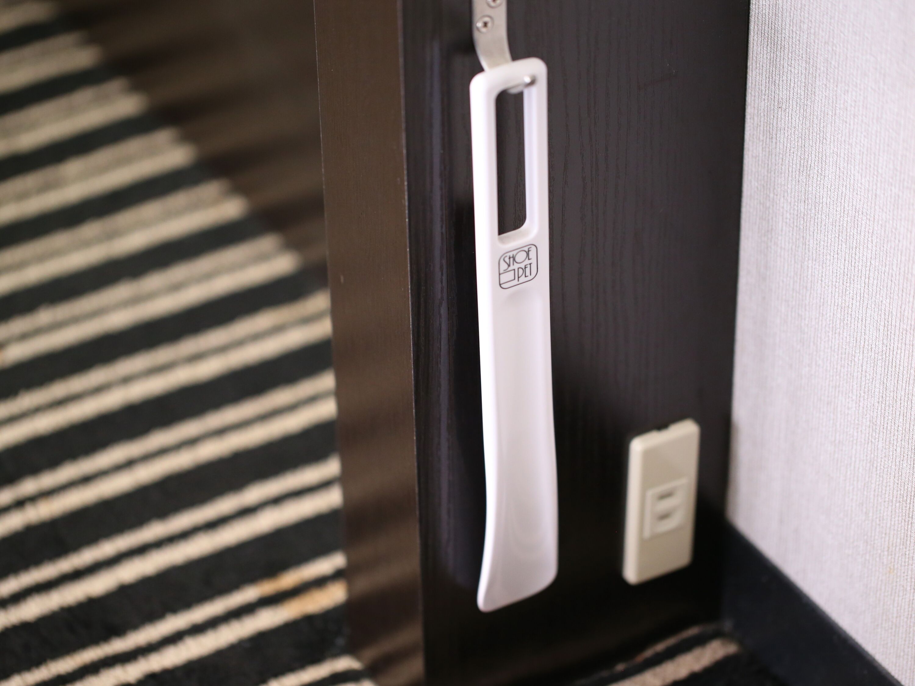 A door with a white handle and a shoe pedal, a power outlet, and a striped carpet.