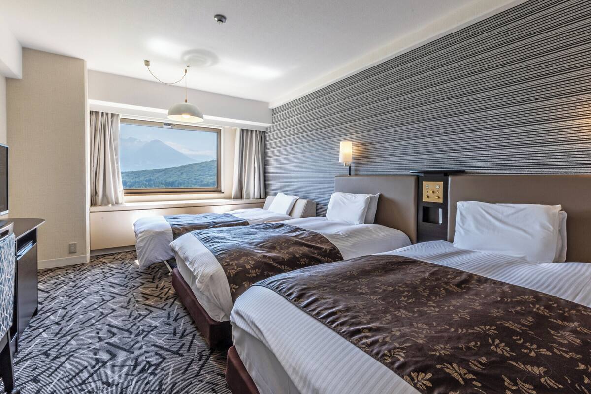 Ein Hotelzimmer mit zwei Betten, einem großen Fenster mit Blick auf die Berge, einem Flachbildfernseher und einem gemusterten Teppich.