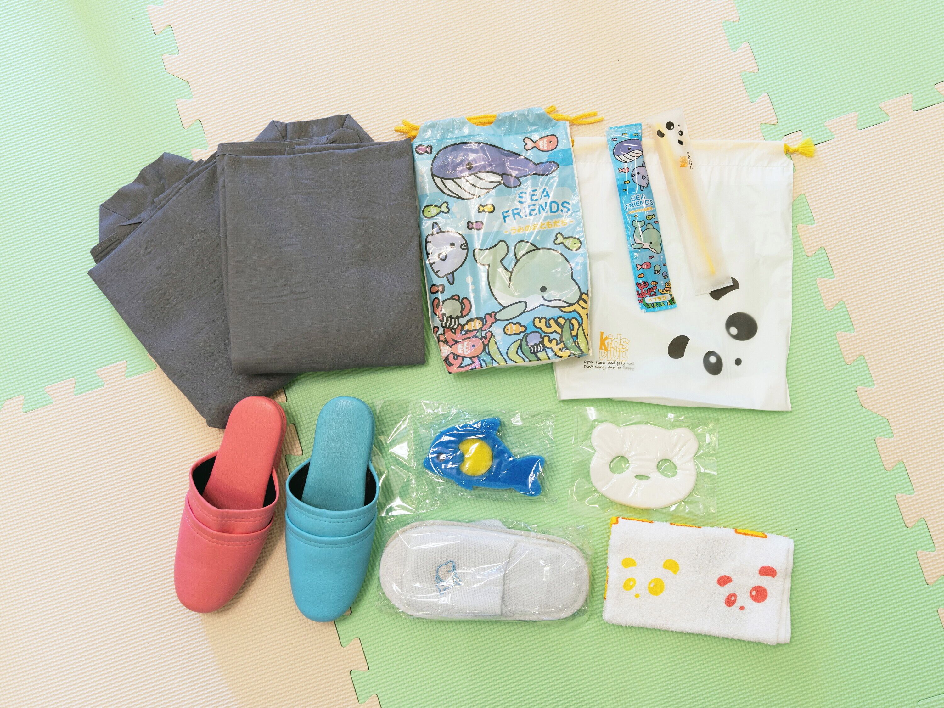 A collection of children's items including shoes, a water bottle, a snack pouch, and a toy on a green mat.