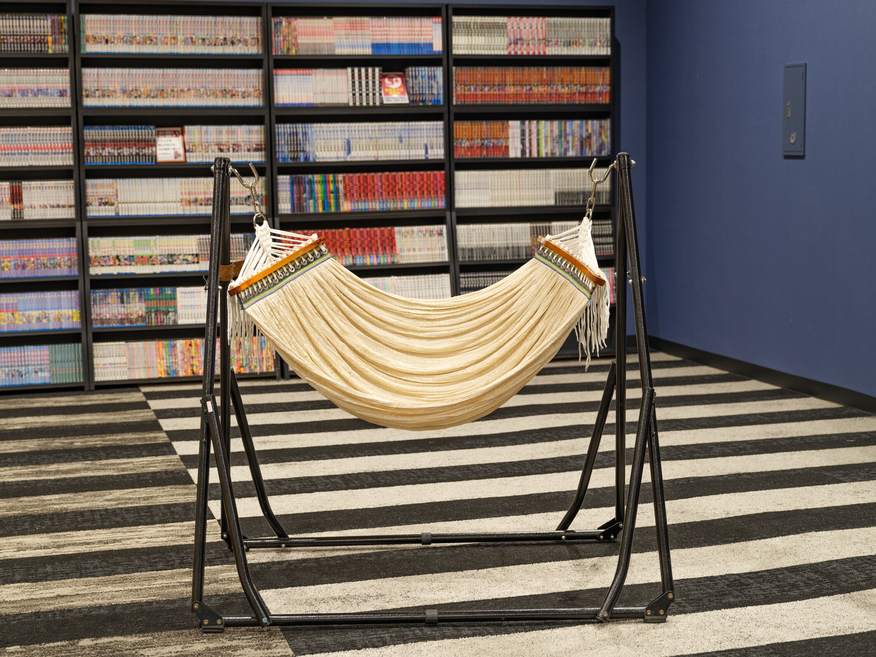 A hammock in a room with a striped floor and a bookshelf in the background.
