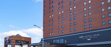 A multi-story hotel with a prominent sign for APA HOTEL STAY (TOYAMA) at the ground level.