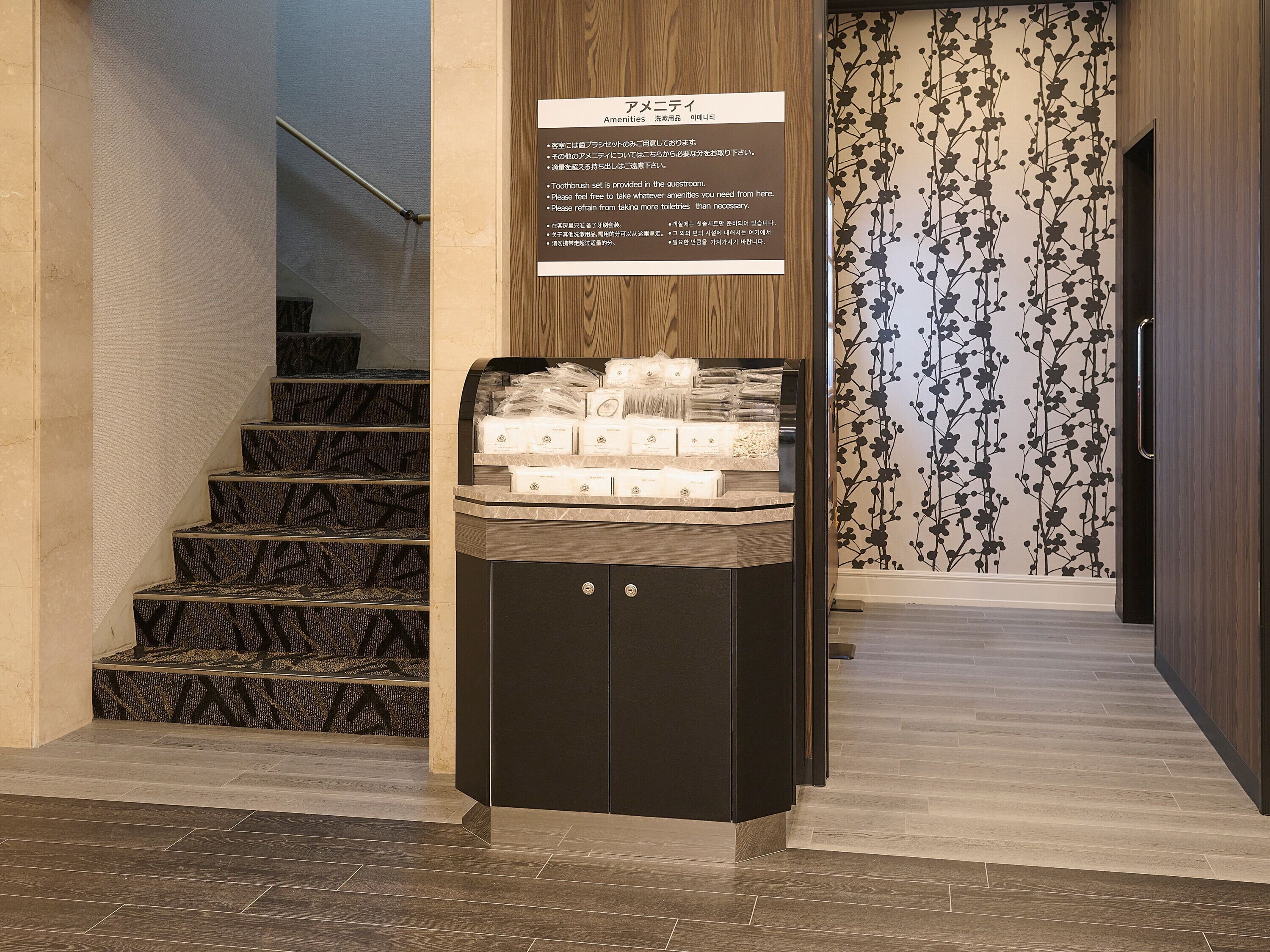 A hotel entrance with a signboard in Japanese, a staircase, and a display of toiletries.