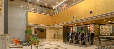 A spacious lobby with a check-in counter, seating area, and a staircase leading to an upper level.