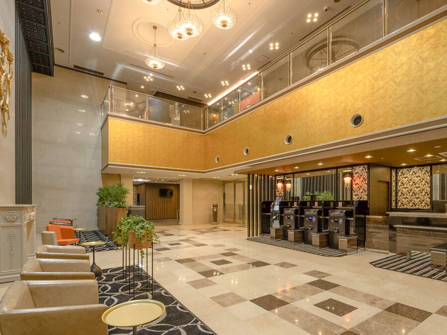A spacious lobby with a check-in counter, seating area, and a staircase leading to an upper level.