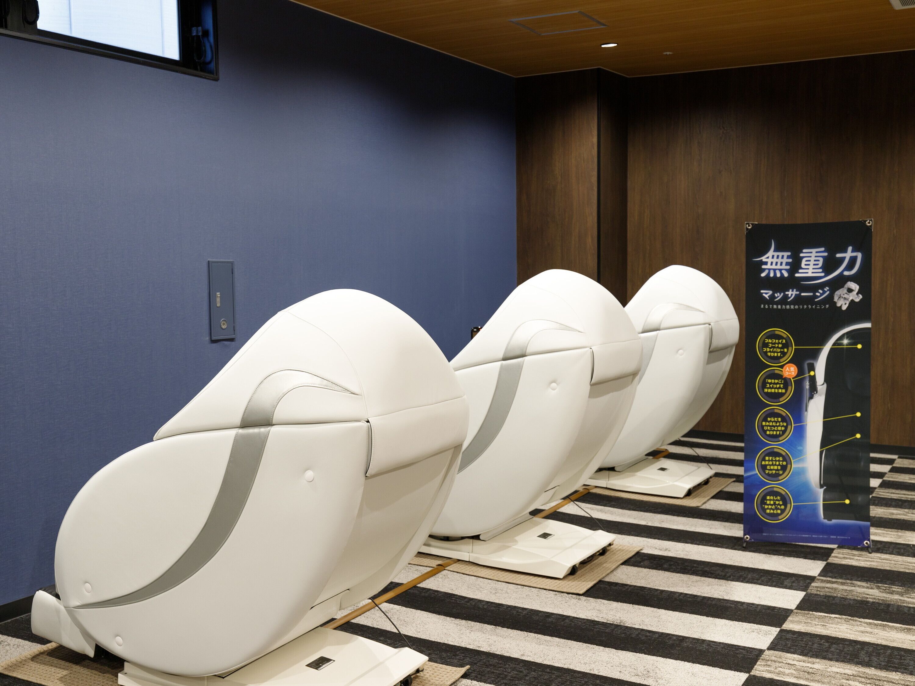 A row of white massage chairs in a room with a blue wall and a wooden floor.