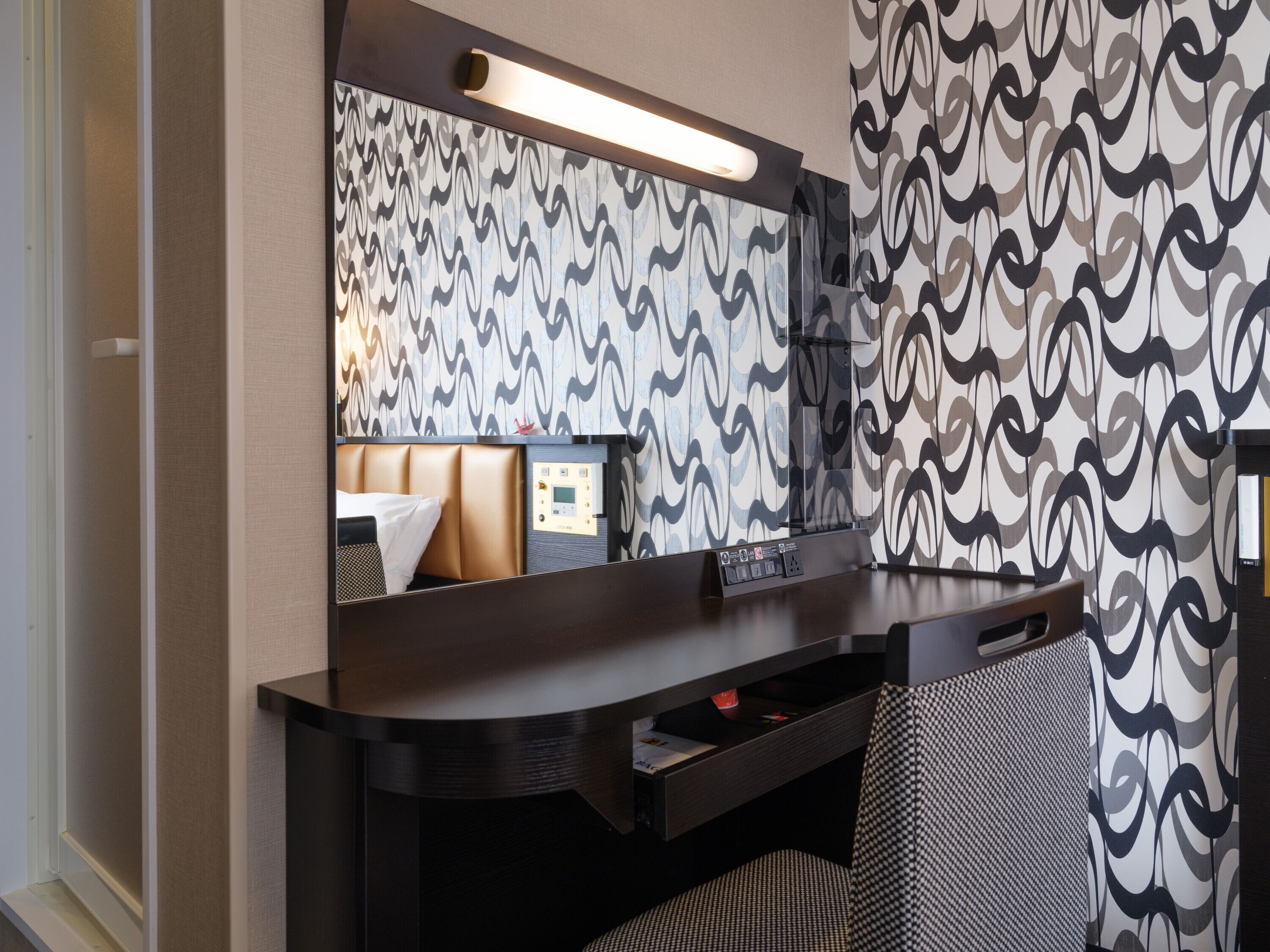Une chambre d’hôtel avec un bureau en bois foncé, un grand miroir et un papier peint à motifs.