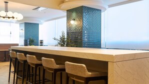 Un área de bar moderna con mostrador de mármol, taburetes de mimbre y una lámpara decorativa.