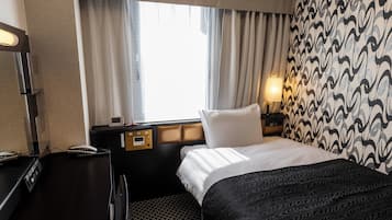 A hotel room with a bed, a desk with a telephone, a control panel, a lamp, and a window with curtains.