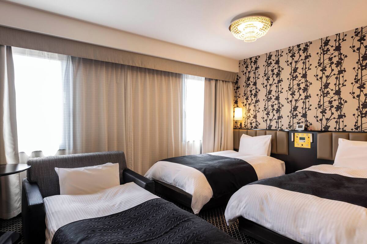 A hotel room with two beds, a desk, and a nightstand with a lamp.