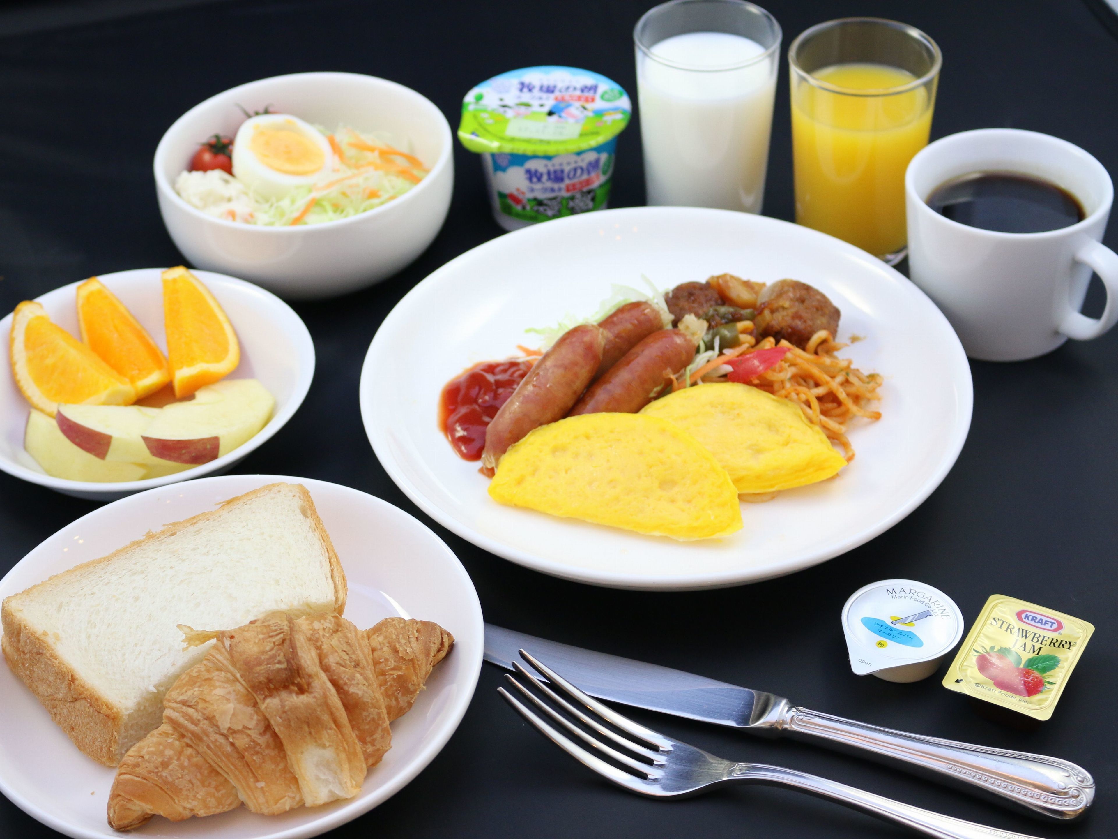 A breakfast table with plates of food, a glass of orange juice, a glass of milk, a cup of coffee, and a fork and knife.