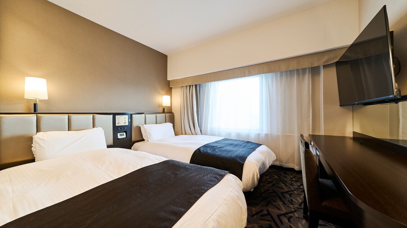 Une chambre d’hôtel avec deux lits, un bureau, une télévision et une fenêtre avec des rideaux.