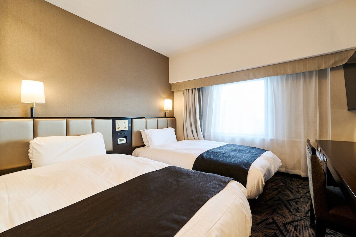 Une chambre d’hôtel avec deux lits, un bureau, une télévision et une fenêtre avec des rideaux.