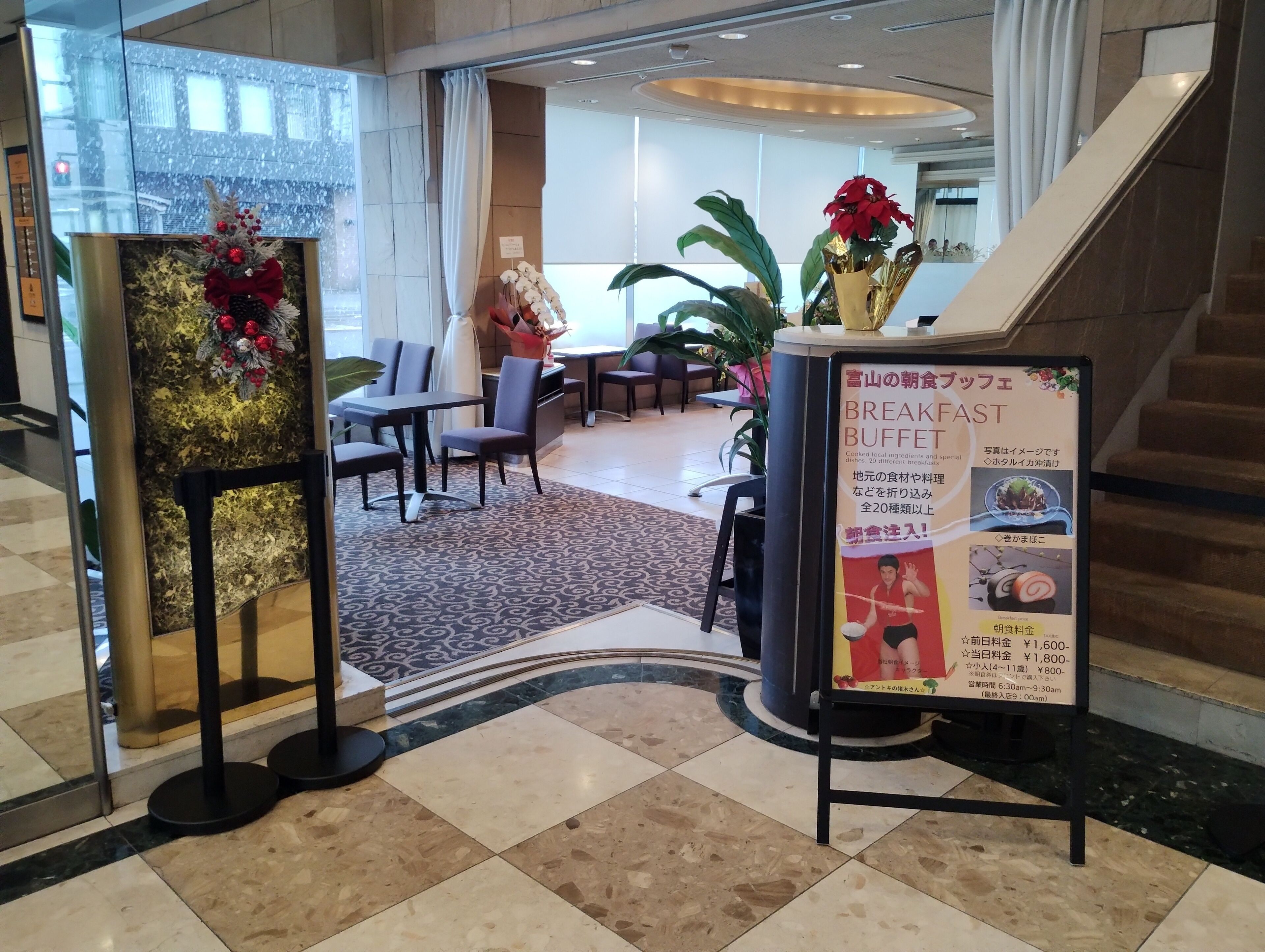 A hotel lobby with a breakfast buffet sign, seating area, and a staircase.