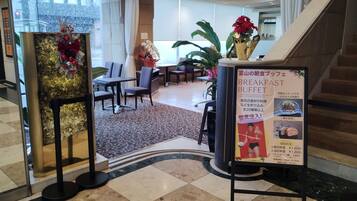 A hotel lobby with a breakfast buffet sign, seating area, and a staircase.