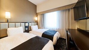 Een hotelkamer met twee bedden, een bureau, een televisie en een raam met gordijnen.