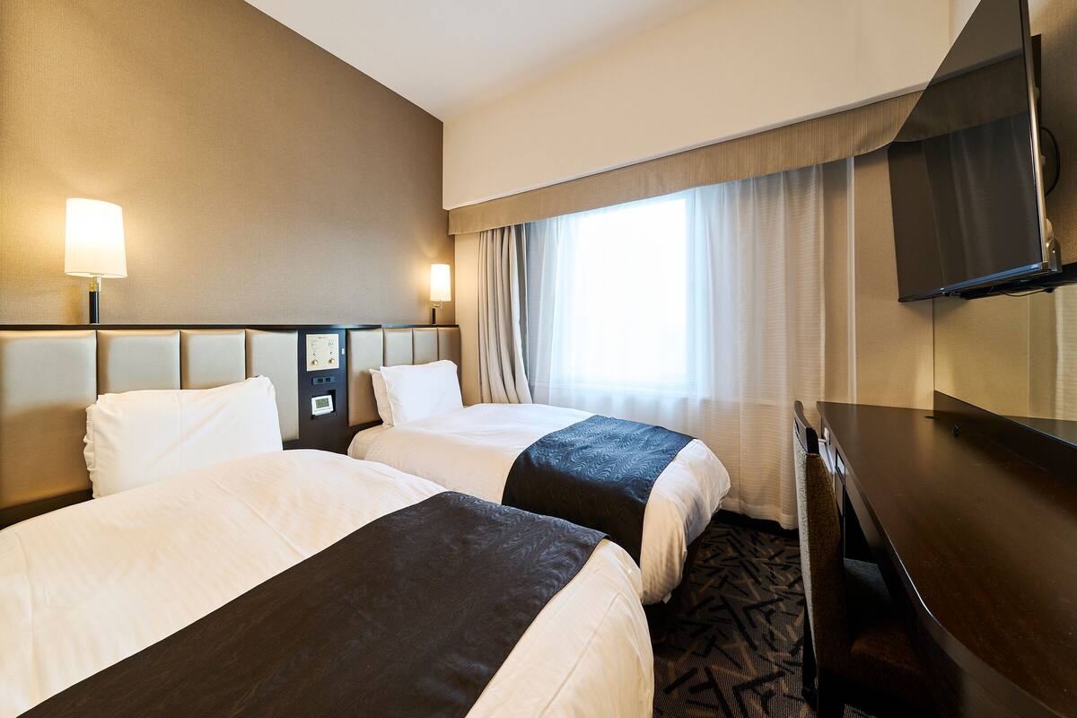 Een hotelkamer met twee bedden, een bureau, een televisie en een raam met gordijnen.