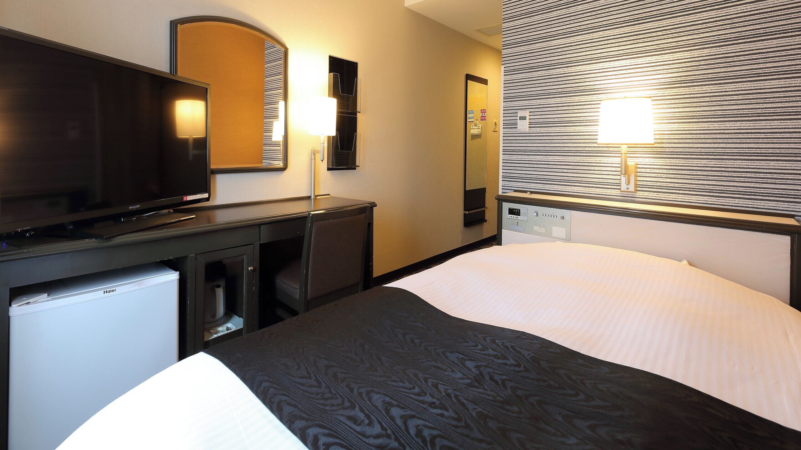 Hotelkamer met een bed, een bureau met televisie, een spiegel en een wandlamp.
