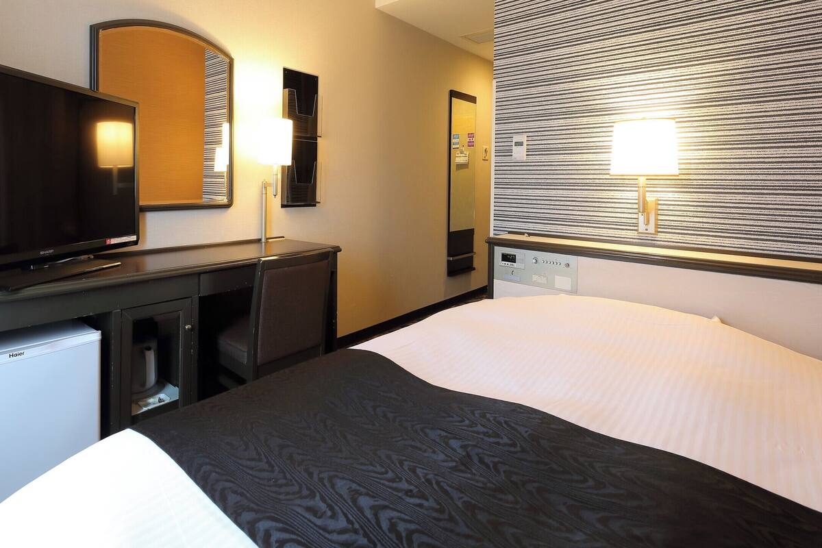 Hotelkamer met een bed, een bureau met televisie, een spiegel en een wandlamp.