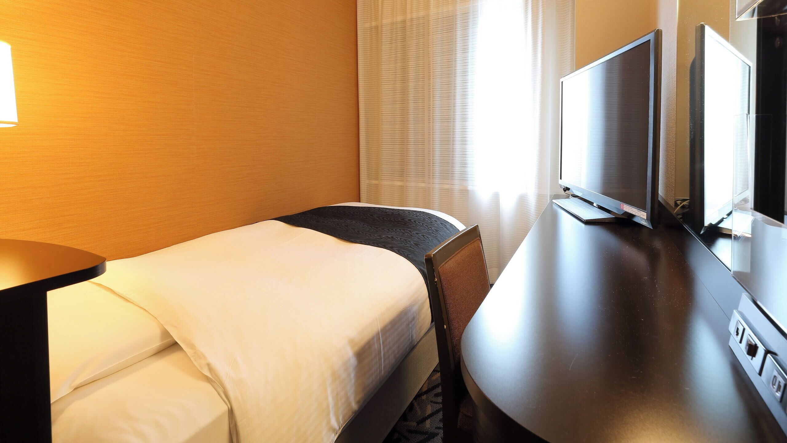 Een hotelkamer met een bed, bureau, televisie en een raam met gordijnen.