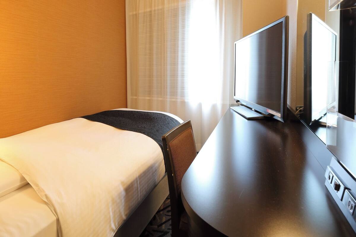 Een hotelkamer met een bed, bureau, televisie en een raam met gordijnen.