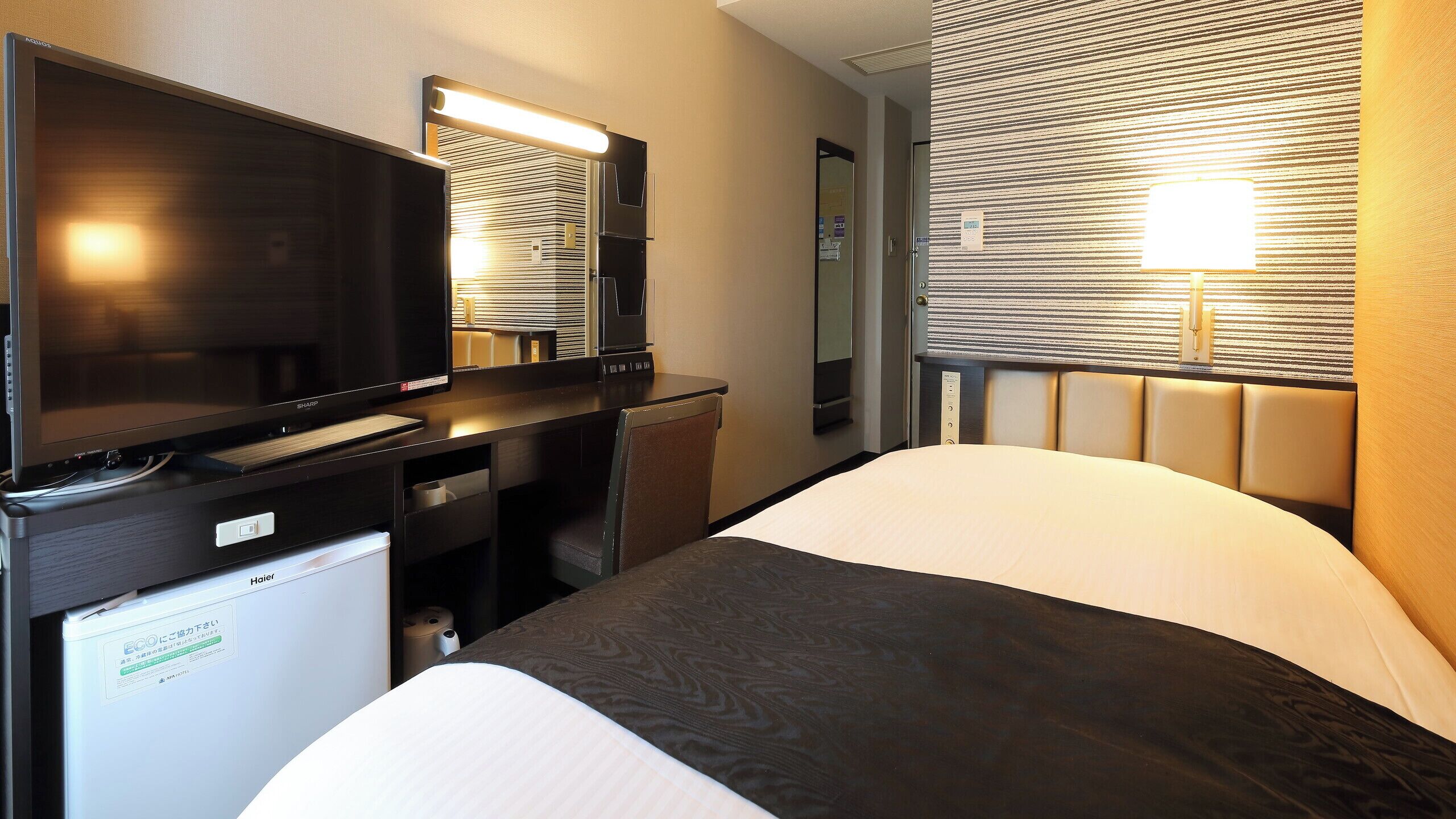 Een hotelkamer met een bed, een bureau met een televisie, een spiegel en een raam met jaloezieën.