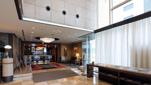 Een hotel lobby met een zwart-wit geruite vloer, een receptiebalie, een zithoek en een groot raam met gordijnen.