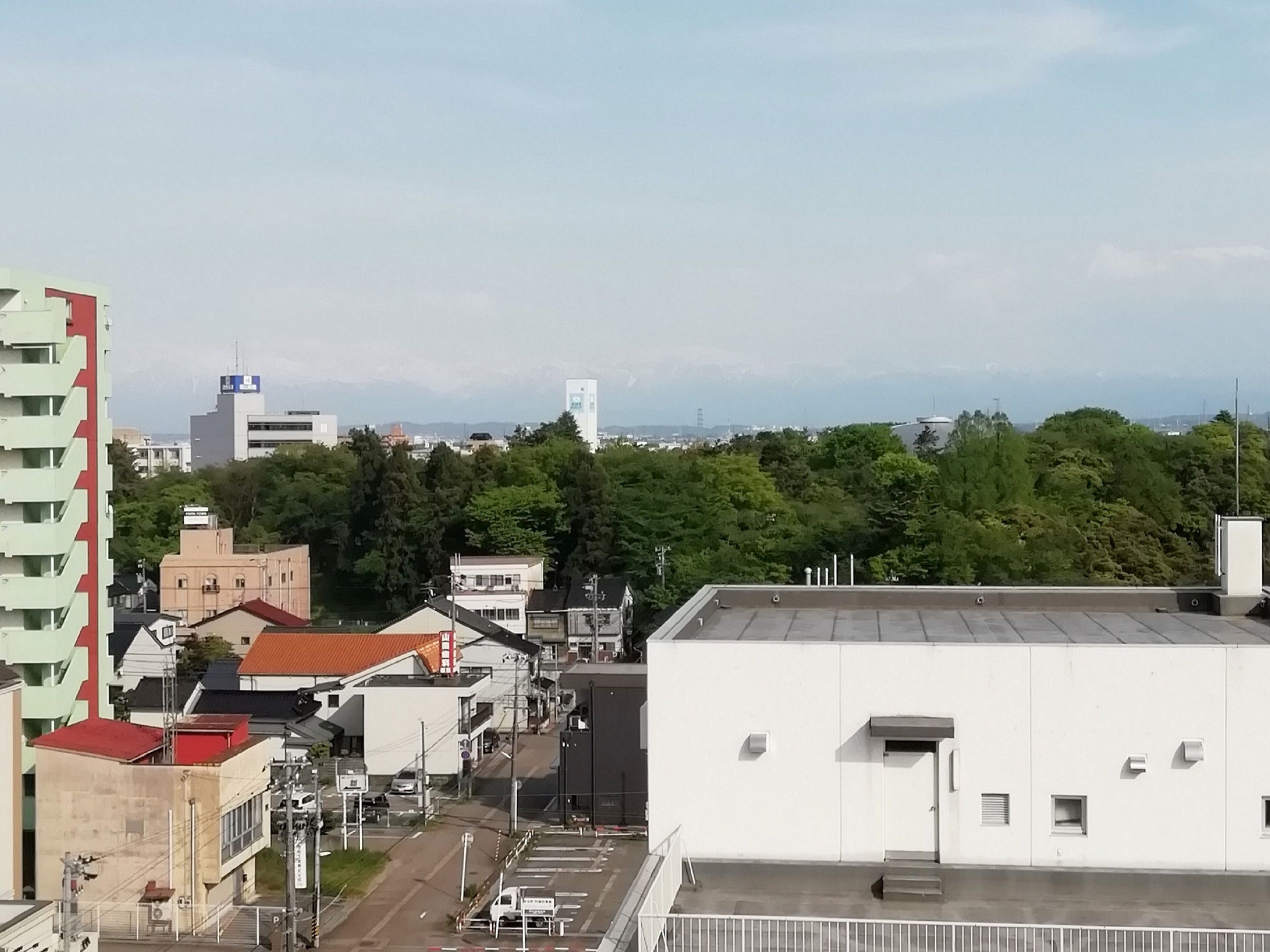 A cityscape with a mix of modern and traditional buildings, a clear sky, and distant mountains.