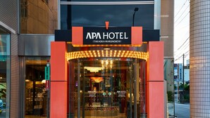 L’extérieur de l’hôtel APA présente une façade vitrée et une enseigne lumineuse.
