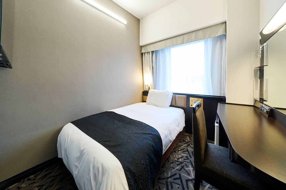 Een hotelkamer met een bed, een bureau, een stoel, een raam met gordijnen en een flatscreen televisie.