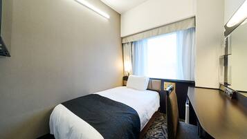 A hotel room with a bed, a desk, a chair, a window with curtains, and a flat-screen TV.