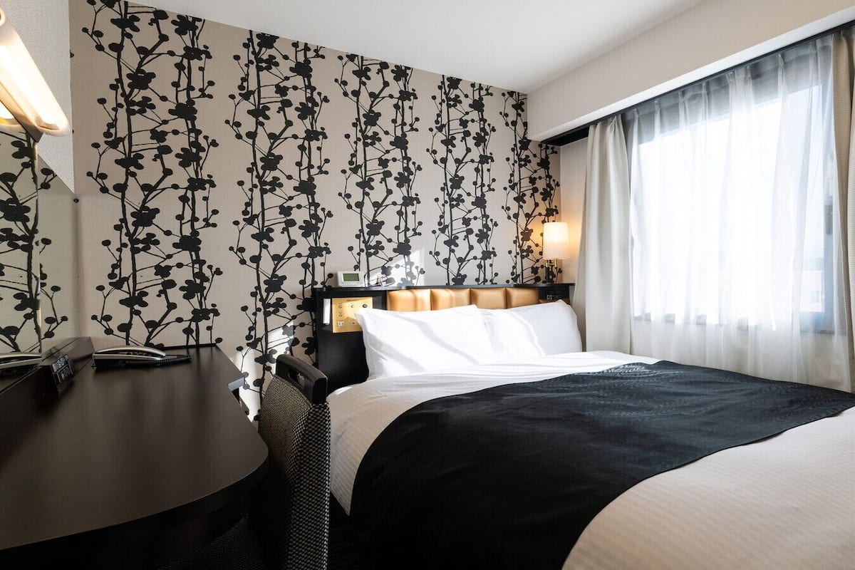 Ein Hotelzimmer mit Bett, Nachttisch, Lampe und einer Wand mit floralem Muster.