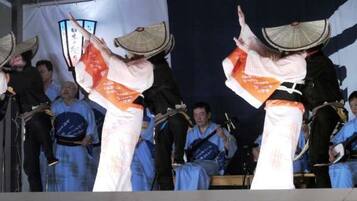 A stage with performers in traditional attire, a crowd of spectators, and a backdrop with Japanese characters.