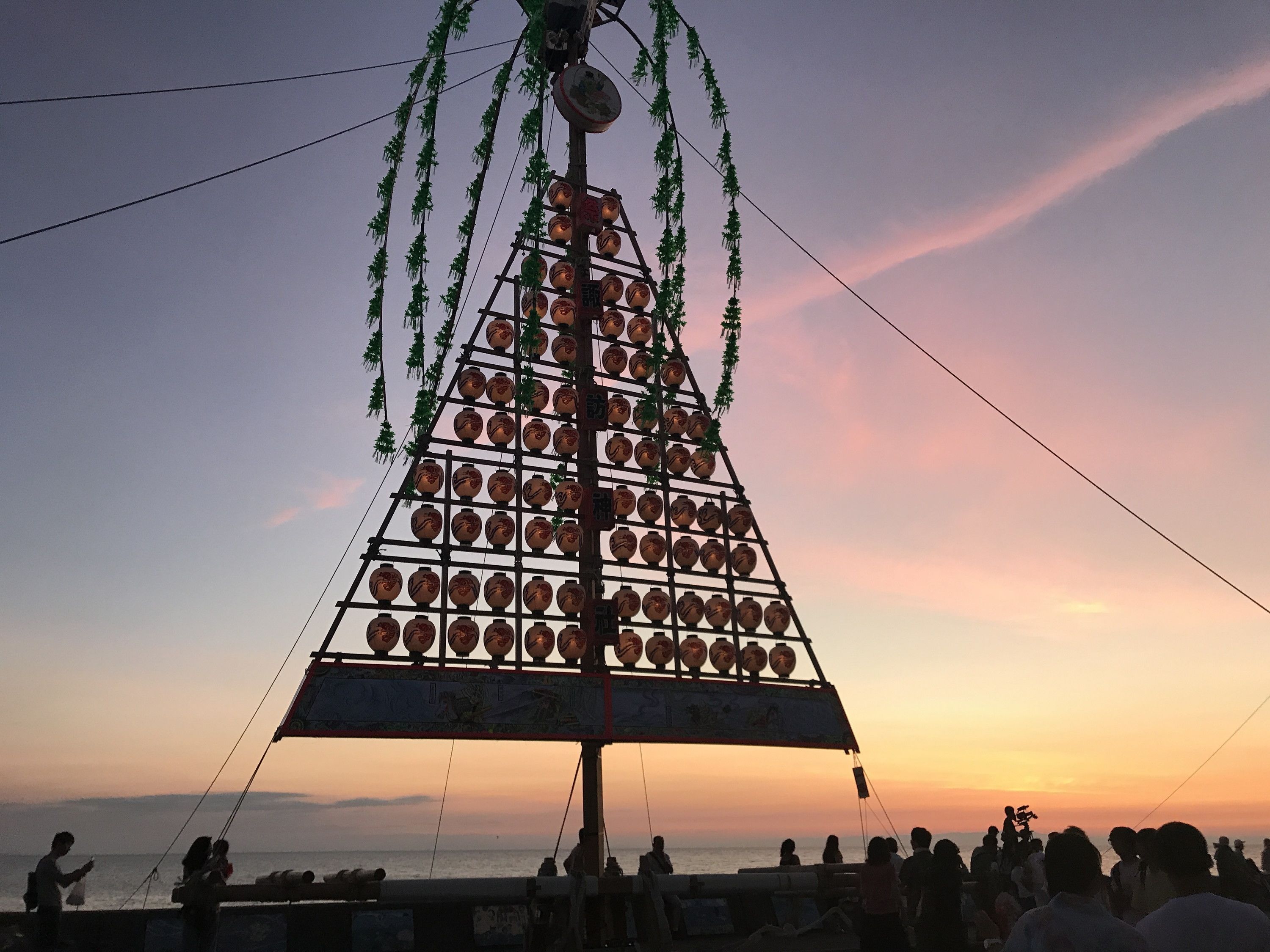 A large, triangular structure with multiple circular elements, possibly a decorative installation, set against a sunset sky.