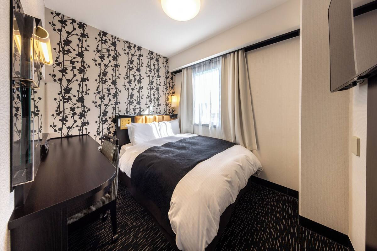 A hotel room with a bed, a desk, a chair, a TV, and a window with curtains.