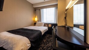 Habitación de hotel con cama, escritorio, silla, lámpara, ventana con cortinas y espejo.