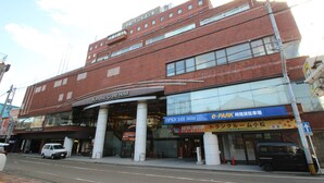 Un edificio de varios pisos con un cartel que dice 'Komatsu Grand Hotel' y un letrero de estacionamiento que indica 'ABIERTO 24H 365B'.